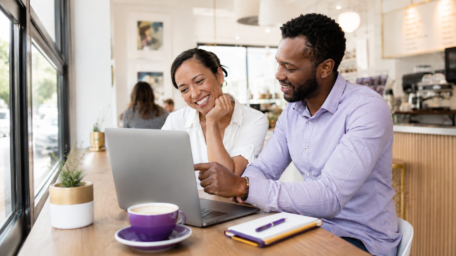 Two people reviewing marketing performance on a laptop in a bright cafe
